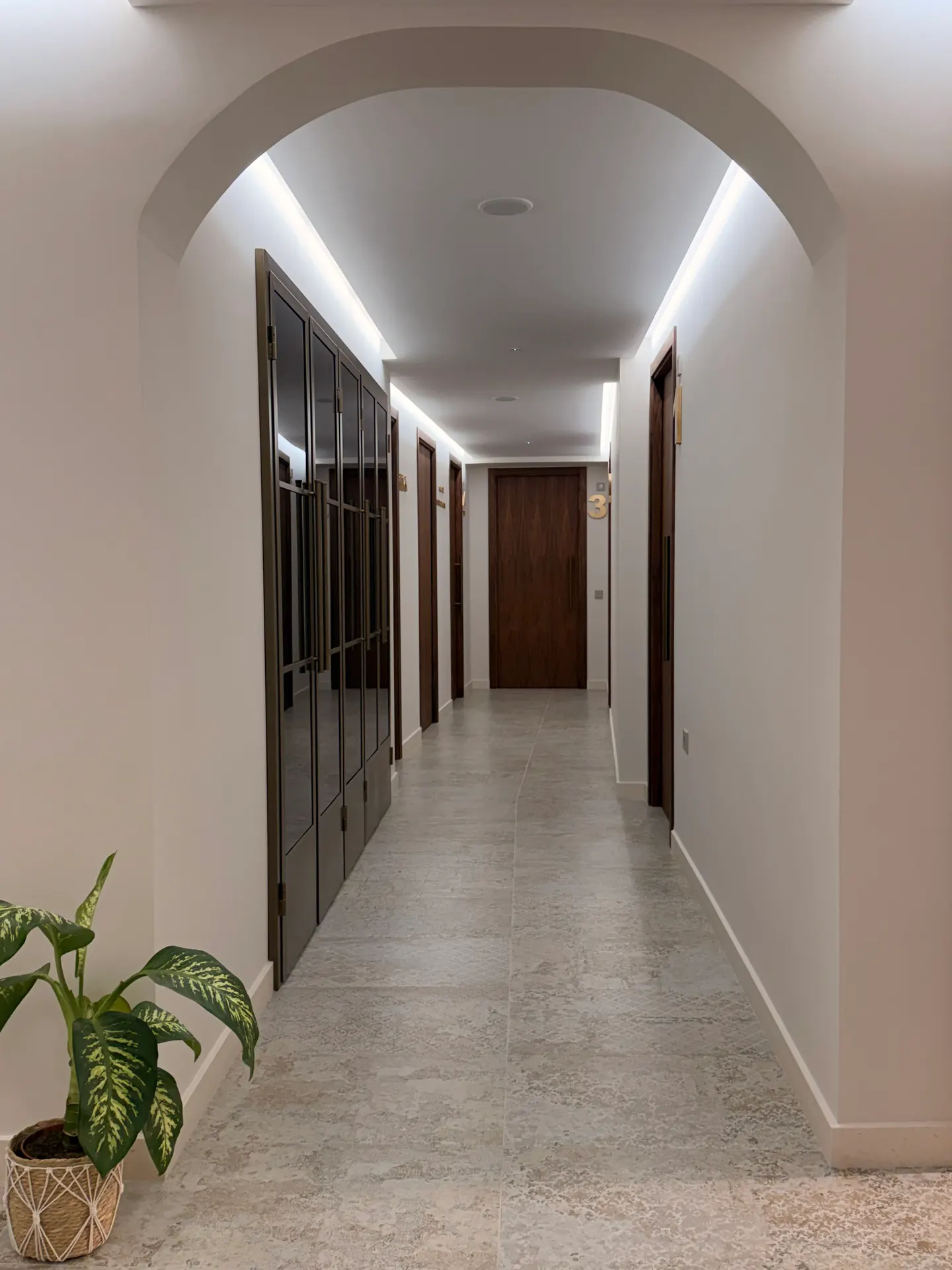 Pasillo de acceso a las consultas, con arco de medio punto, puertas de madera de nogal e iluminación indirecta